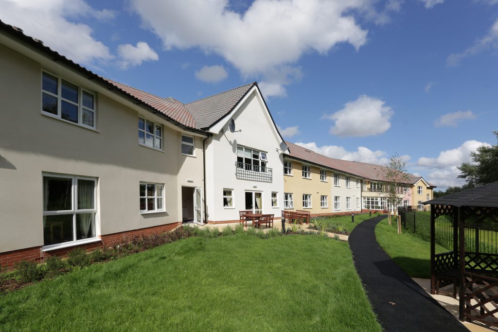 De Lucy House care home exterior with landscaped garden and walkway in daylight
