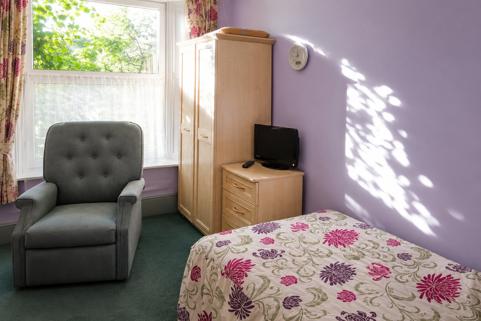Grey armchair, TV and wardrobe in a bright bedroom at The Briars