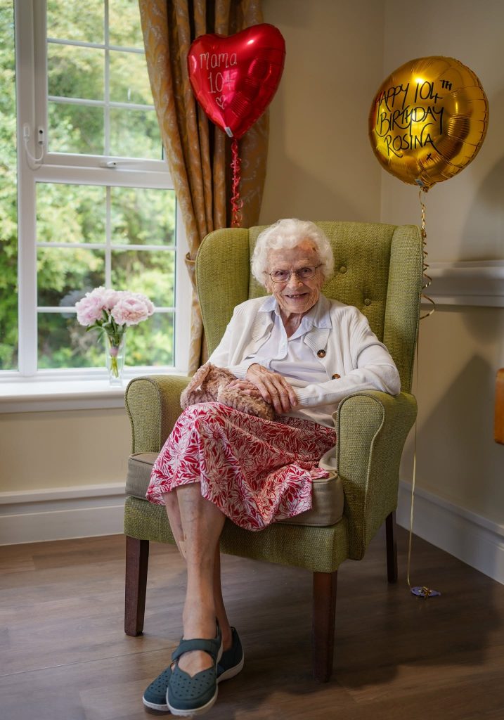Elderly woman celebrating birthday with balloons in care home