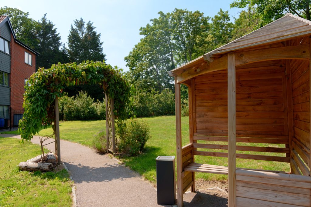 Wooden garden shed with pergola walkway and leafy arch at Henley House Care Home in Ipswich