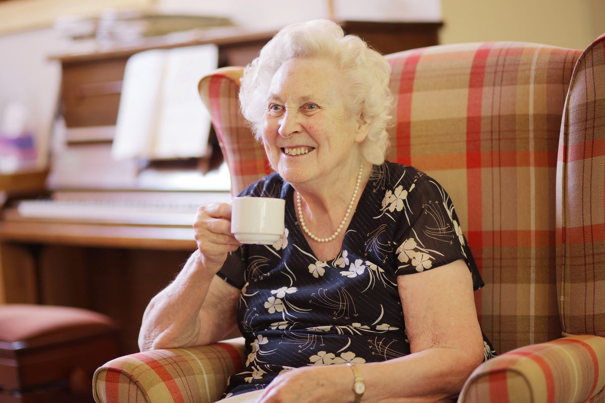 A smiling resident enjoying a cup of tea in an armchair