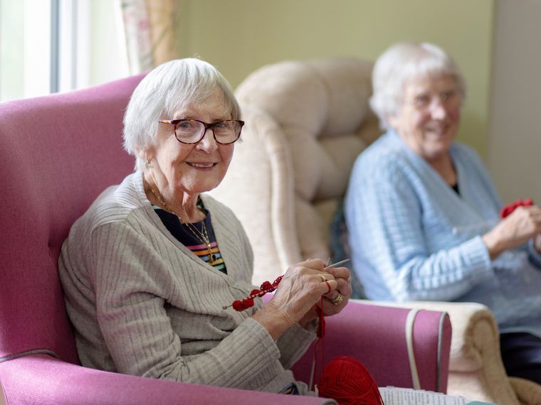 A resident knitting in a sunlit lounge with a colleague alongside